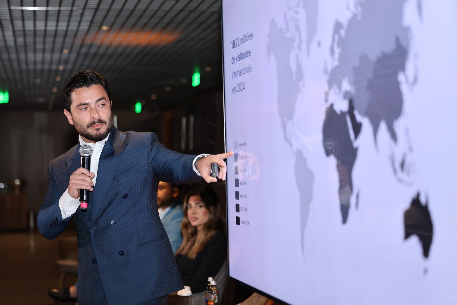 Weverton speaking into a microphone at an event in front of a world map